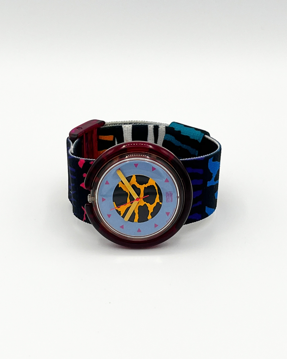 A wristwatch with a patterned strap featuring blue, black, and red tones, a translucent red case, and a light blue dial with yellow hands and a central yellow graphic.