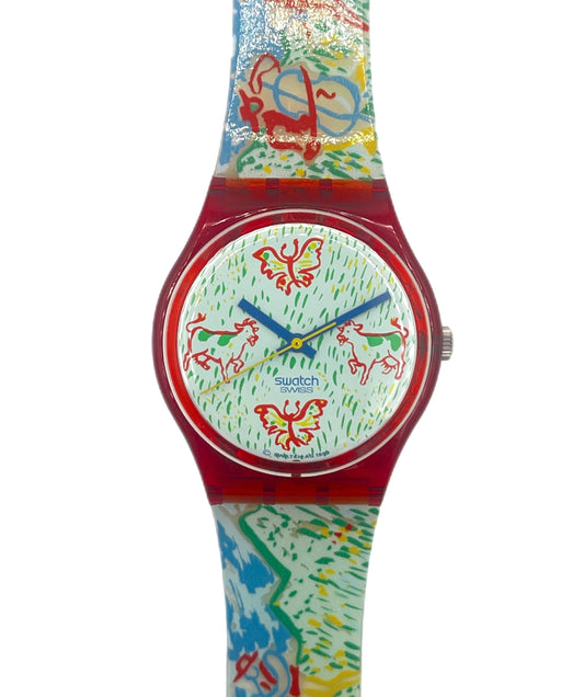 A Swatch wristwatch featuring a vibrant, multicolored abstract pattern on the strap and dial, with a translucent red case and blue hands.