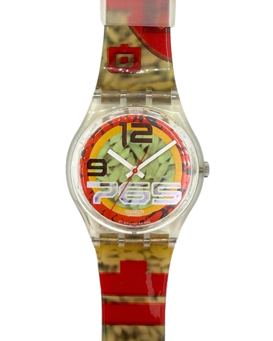 A Swatch wristwatch with a clear plastic case and a colorful patterned strap featuring red, yellow, and brown abstract designs. The dial has a red, yellow, and green graphic with black and white numerals.