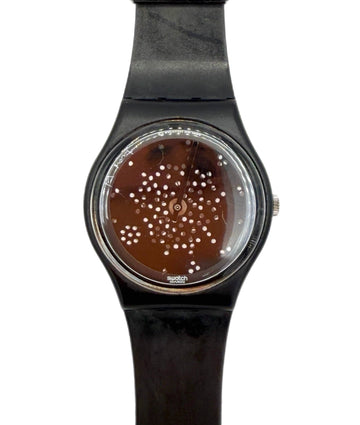 A Swatch wristwatch with a black strap and case, featuring a brown dial decorated with a pattern of small white dots.