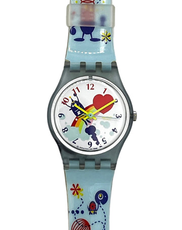 A Swatch wristwatch featuring a light blue silicone strap and case with a whimsical multicolor cartoon design, including a red heart, blue characters, and yellow stars on a white dial.