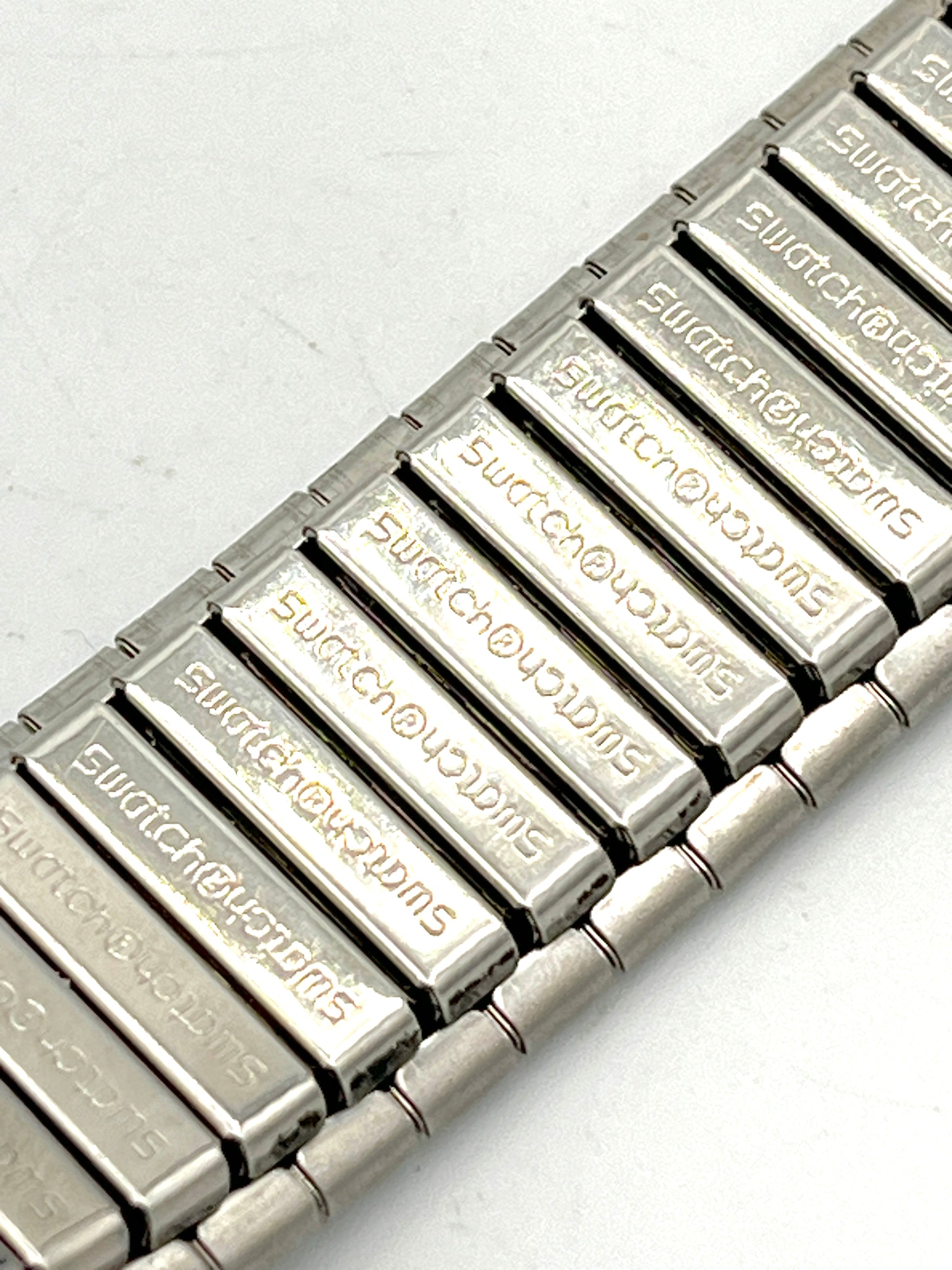 Metallic watch strap with 'Swatch' branding on a white background