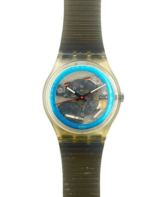 A Swatch wristwatch with a translucent olive green strap, a clear case, and a blue inner bezel around a dark mechanical dial.