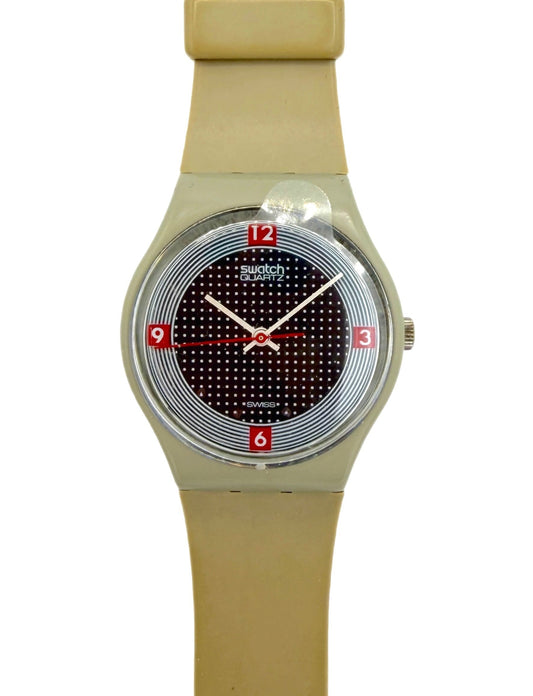 A Swatch analog watch with a beige silicone strap, a silver-toned case, and a black dotted dial with red numerals.