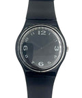A Swatch wristwatch with a black silicone strap, black dial, and silver-tone bezel, shown against a plain white background.