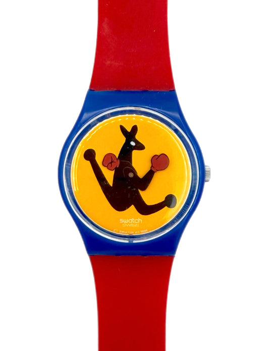 A Swatch wristwatch with a bright red silicone strap, a blue bezel, and a yellow dial featuring a black kangaroo holding red boxing gloves.