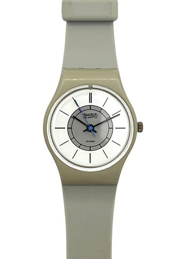 A Swatch wristwatch with a light gray silicone strap, a beige-toned case, and a white dial featuring blue hands and a gray inner ring.