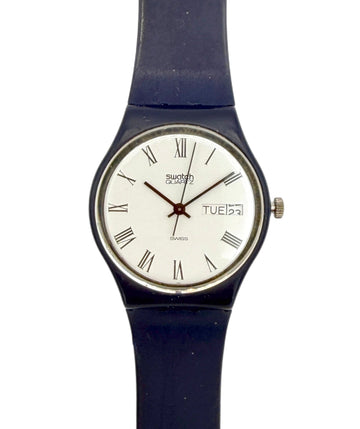 A Swatch wristwatch with a dark blue strap, a silver-tone case, and a white dial featuring black Roman numerals and a day window.