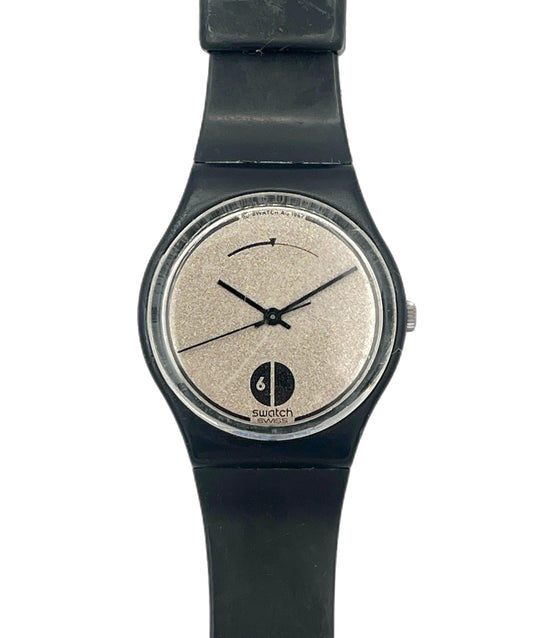A Swatch watch with a black strap and case, featuring a textured beige dial with black hands and a black logo at the bottom.