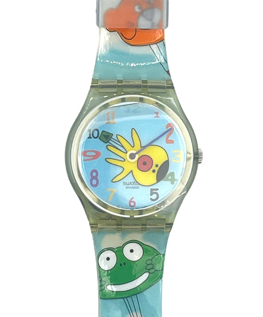 A children's wristwatch with a light blue strap featuring cartoon graphics, including a yellow sun and a green frog in a hot air balloon. The watch has a clear case and a round dial with colorful numbers.