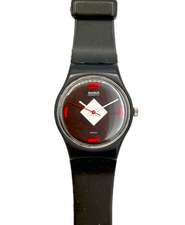A Swatch Swatch Classic wristwatch with a black silicone strap, black case, and a dark brown dial featuring a white diamond logo and red accents.