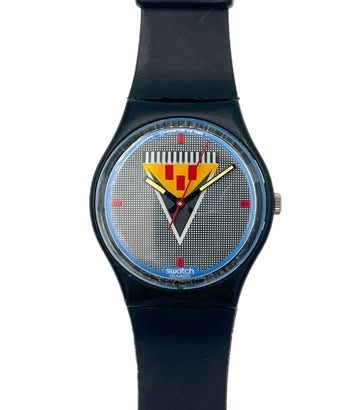 A Swatch wristwatch with a black strap and case, featuring a textured silver-gray dial with a yellow and red striped shield logo and blue accents.