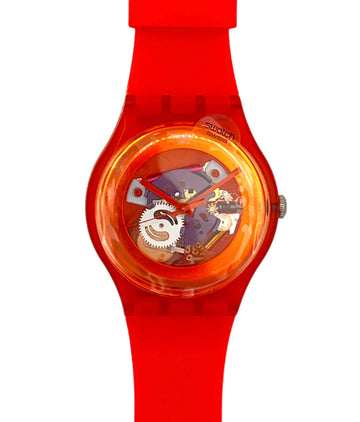 A Swatch wristwatch featuring a bright red silicone strap and case, with a transparent dial showing colorful internal mechanical details.