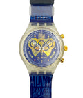 A Swatch wristwatch featuring a blue strap with 'ATLANTA BARCELONA FEST' text, a gold-tone case, and a blue dial with a yellow and white 1994 Olympic rings graphic.