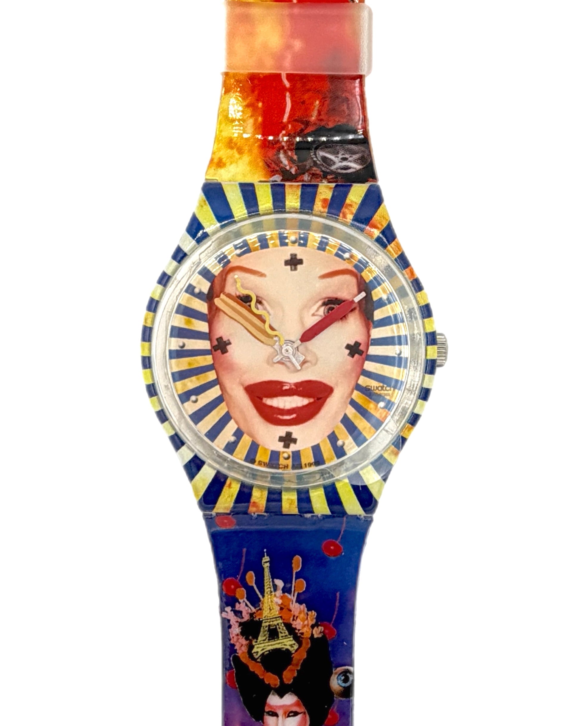 A Swatch wristwatch featuring a colorful Egyptian-themed design with a blue and gold striped dial, a stylized face graphic, and a multicolor strap with red, orange, and blue sections.