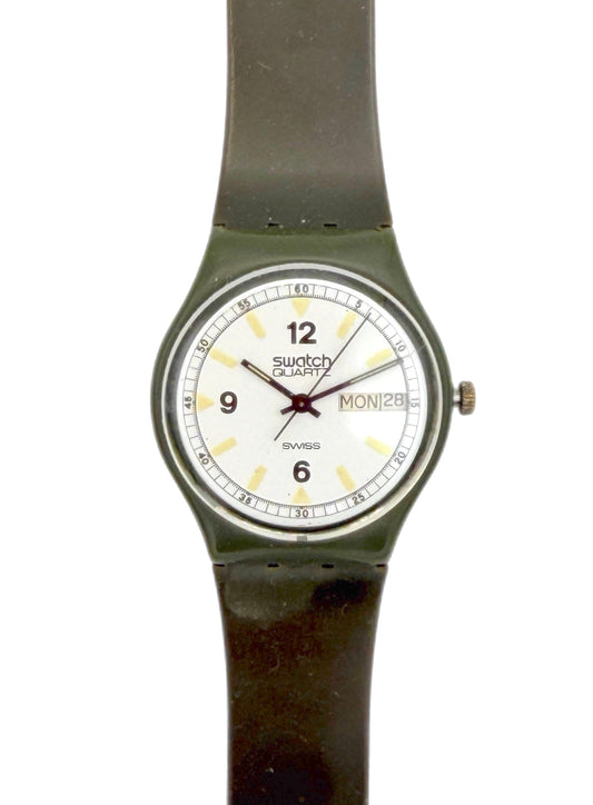 A vintage Swatch Duxx wristwatch with a dark olive green strap and case, featuring a white dial with black Arabic numerals and a day/date window.